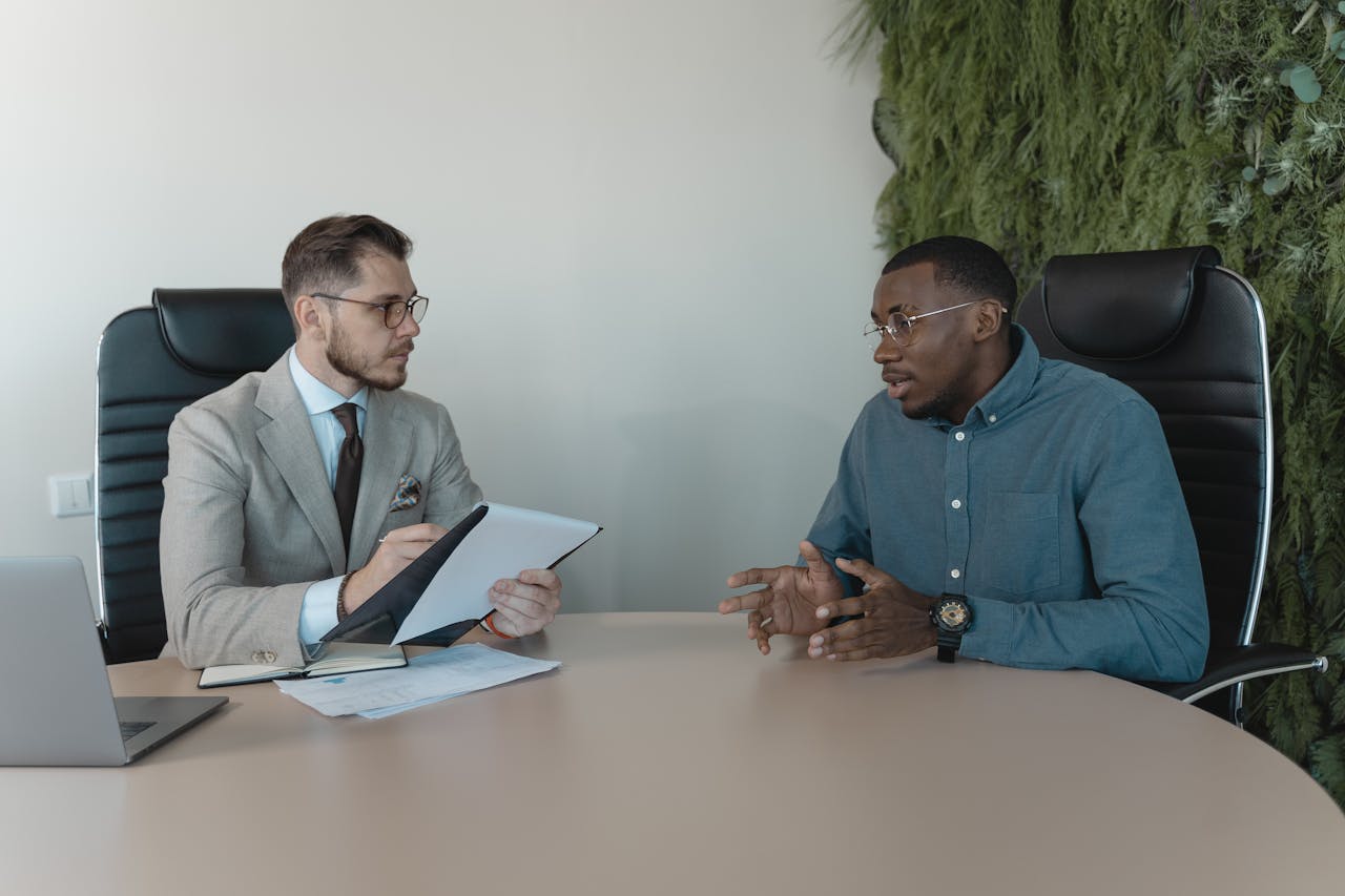 our-experience Two businessmen engaged in a discussion during a job interview in a contemporary office environment.